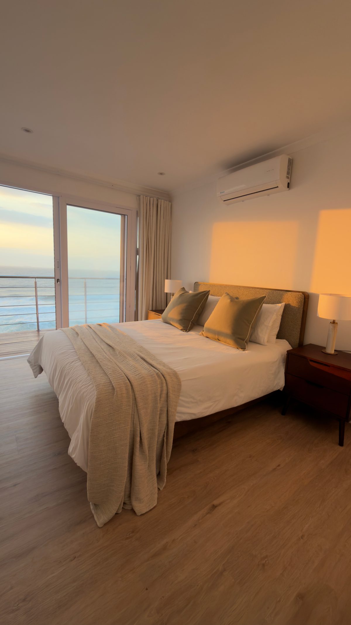 Wide view of the main bedroom, with balcony doors and the sea beyond in warm morning light
