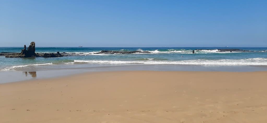 Umdloti tidal pool at low tide, rock shelf and sand under a clear sky