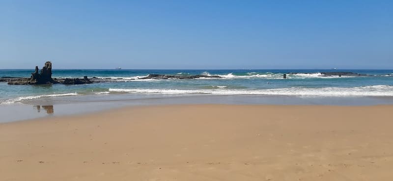 Umdloti tidal pool at low tide, rock shelf and sand under a clear sky